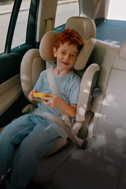 Ein Kind sitzt in einem Kindersitz mit Sitzerhöher im Auto.