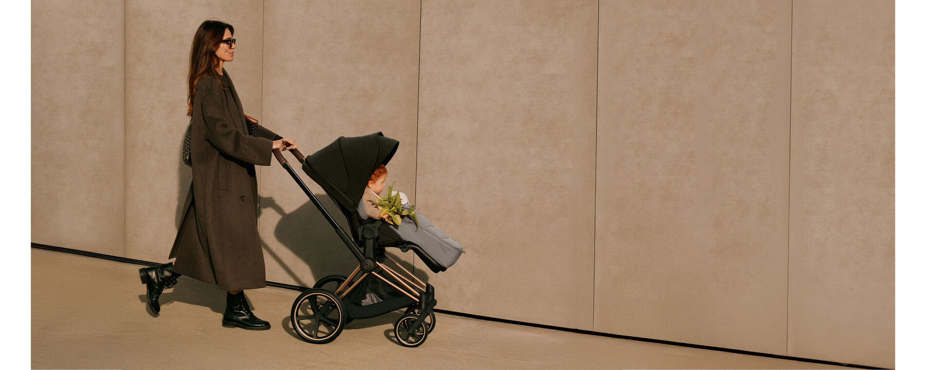 A woman pushing a CYBEX Platinum stroller, her child sitting inside in a footmuff.