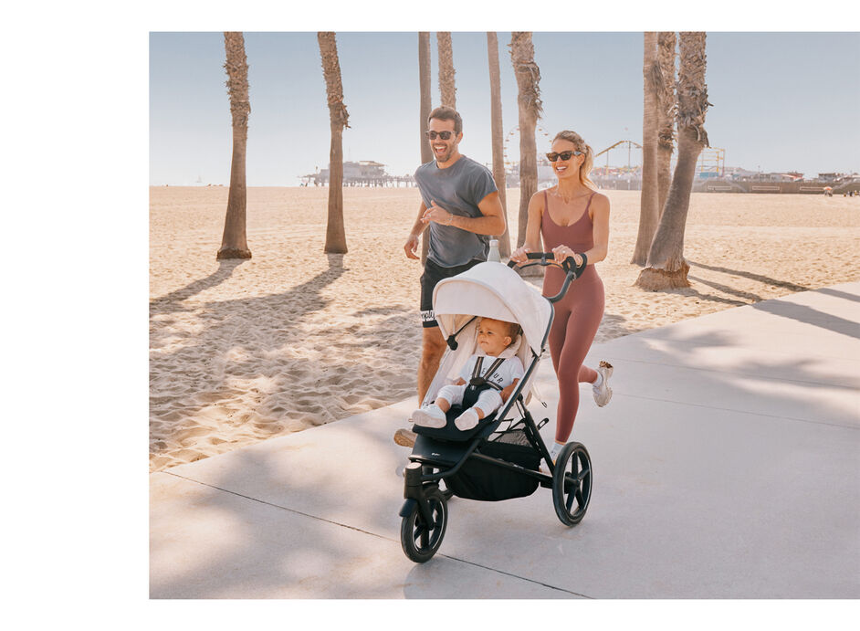Parents pushing their child in an Avi Spin stroller through the sand at the beach.