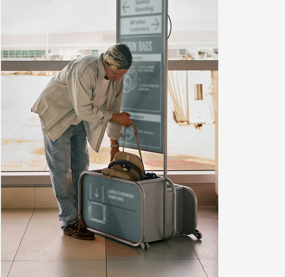 Mann legt den zusammengefalteten kompakten Orfeo Buggy in die Handgep&auml;ck-Messbox am Flughafen