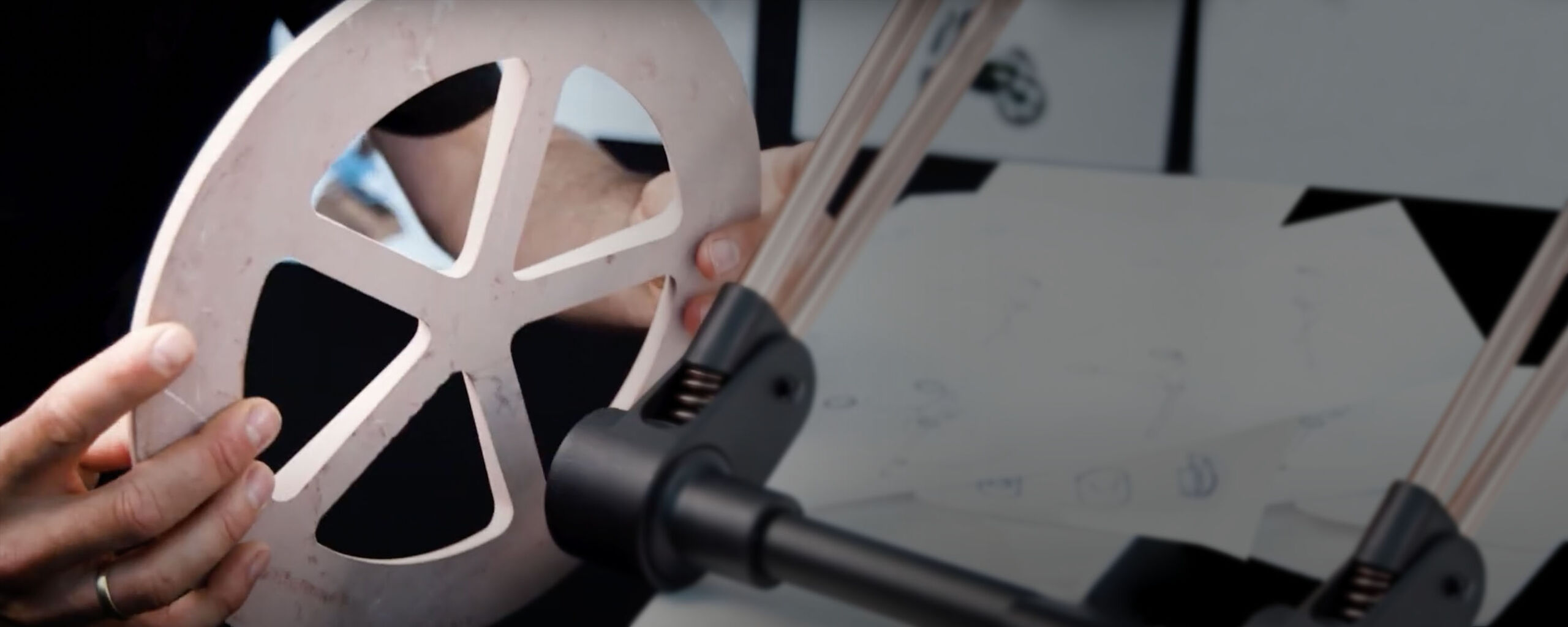 A pair of hands holding a circular part for a pushchair, with the frame of the pushchair in focus and a light, out-of-focus background.