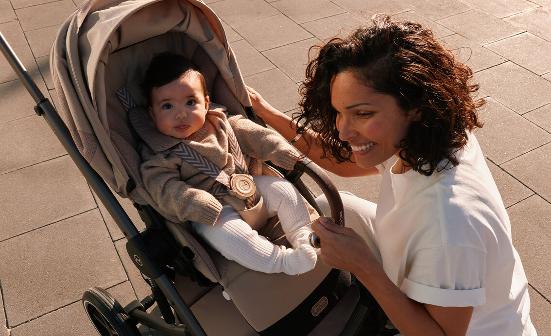 A woman kneeling before her child that is sitting in a Balios S Lux stroller. The baby looks directly in the camera.