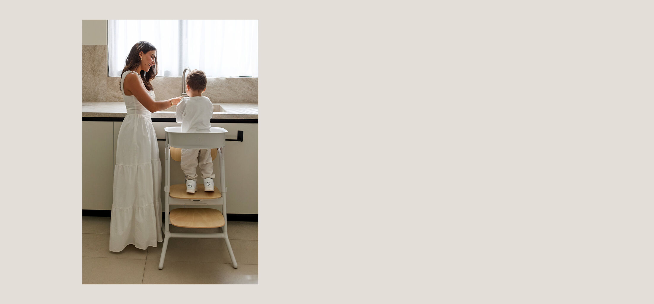 A mother holding her baby with one hand and a CYBEX high chair with the other.