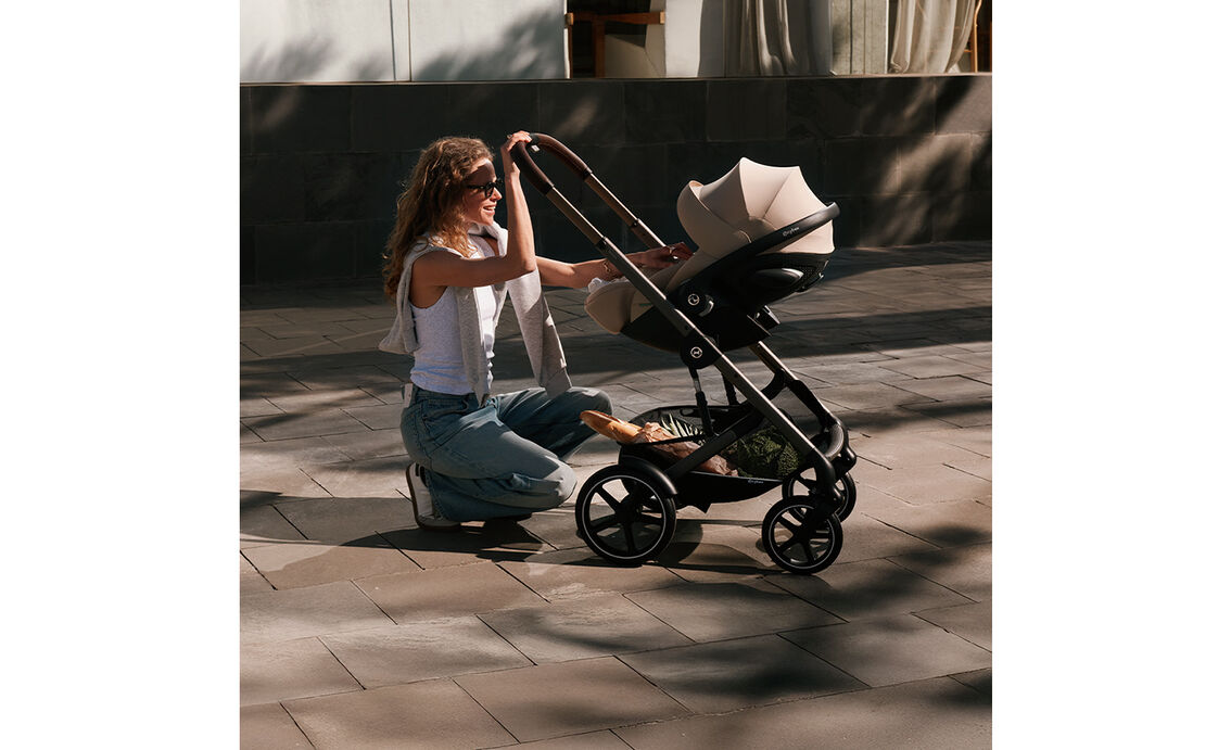 A mother kneeling on a ground and checking on her baby in a Talos S Lux stroller with an infant car seat attached.