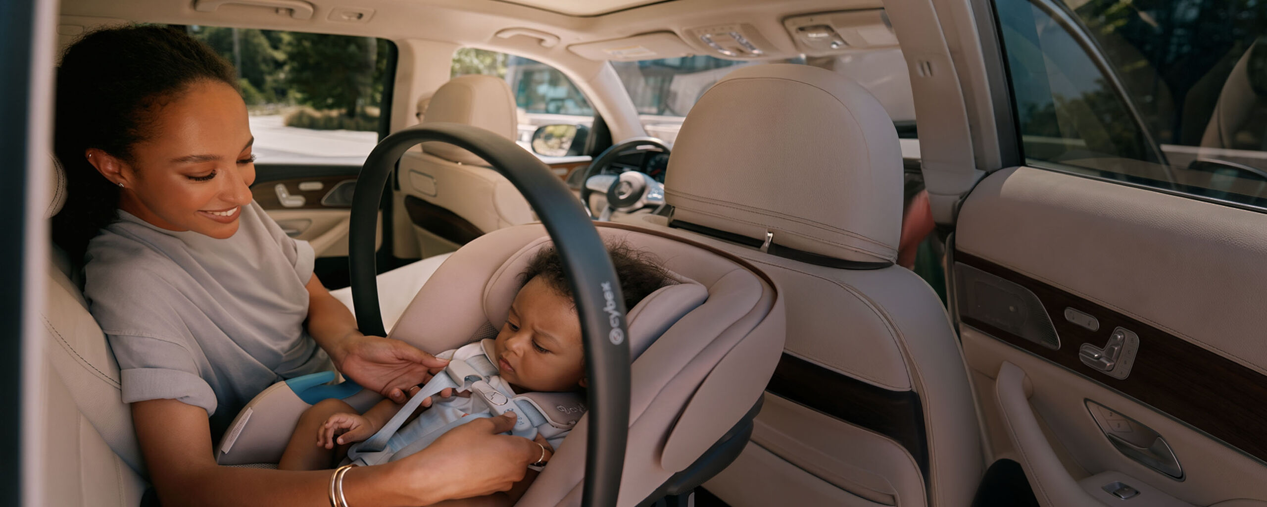 A woman in the back of the car, adjusting the SensorSafe of her child that sits in a CYBEX Gold Car Seat.