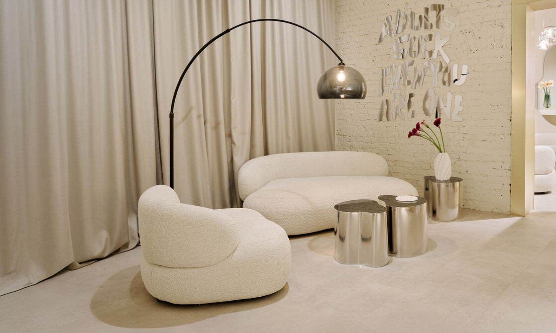 A white couch and an armchair with three coffee tables and a standing lamp.