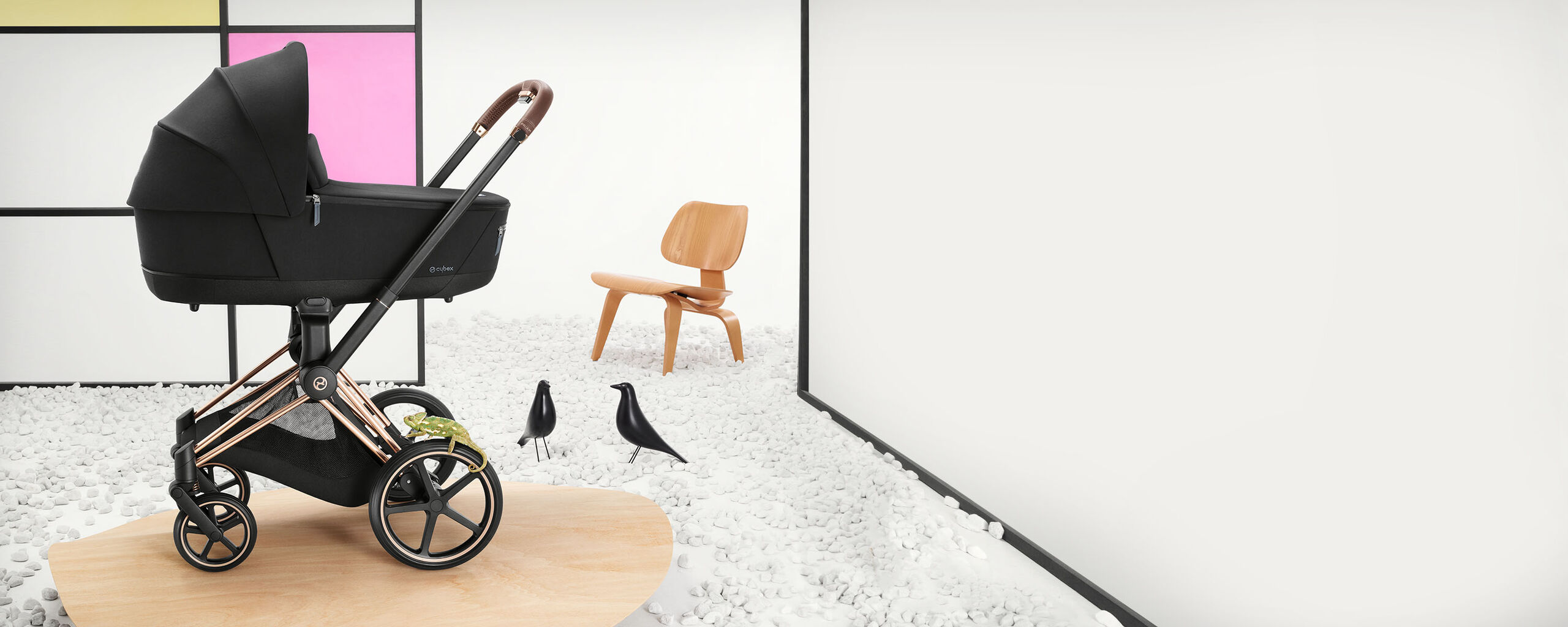 Priam luxury pram in a modern interior with a wooden chair and decorative birds.