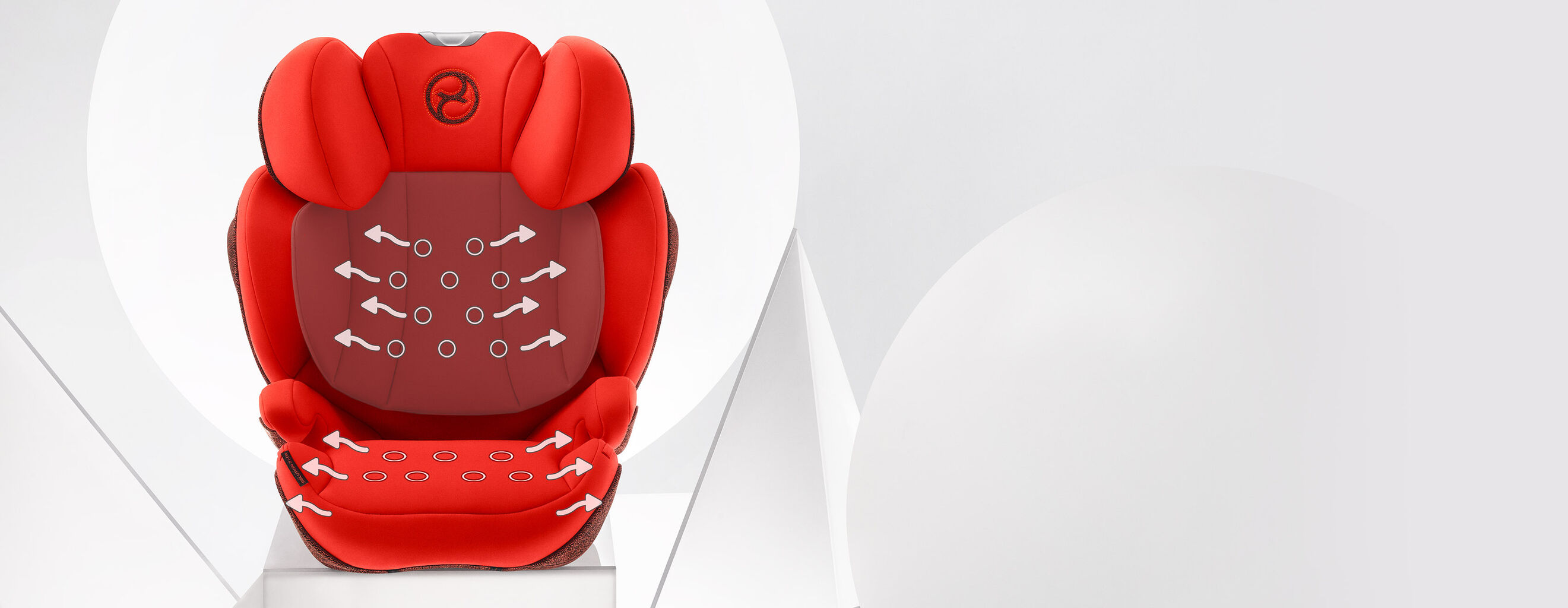 A red child car seat with ergonomic design and ventilation holes highlighted by arrows.