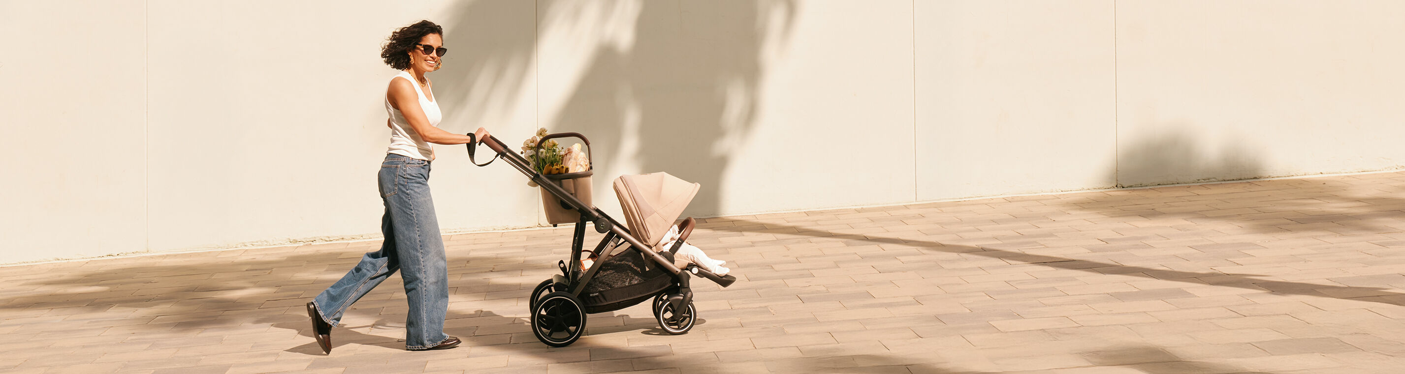 A woman pushing a Gazelle S stroller with a seat pack and a basket.