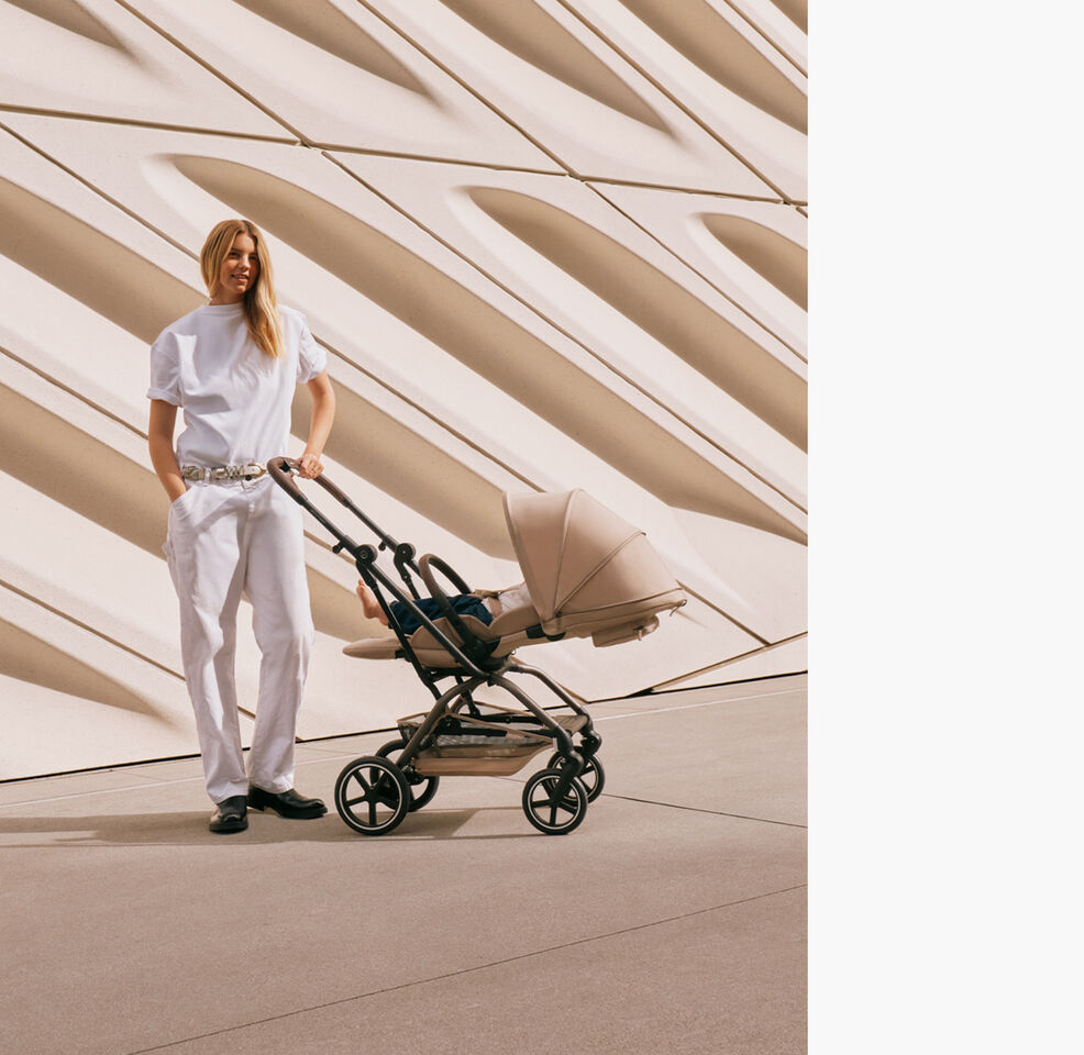 A woman with one hand in the pocket of her pants and the other holding the handlebar of her Eezy S Twist +2 buggy that has been put to a lie-flat position.