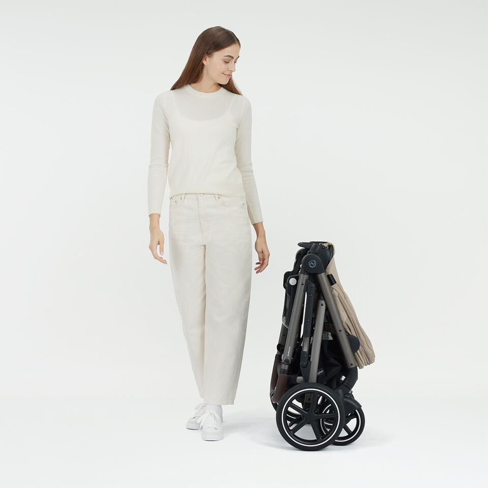 A woman standing next to a folded Gazelle S stroller.
