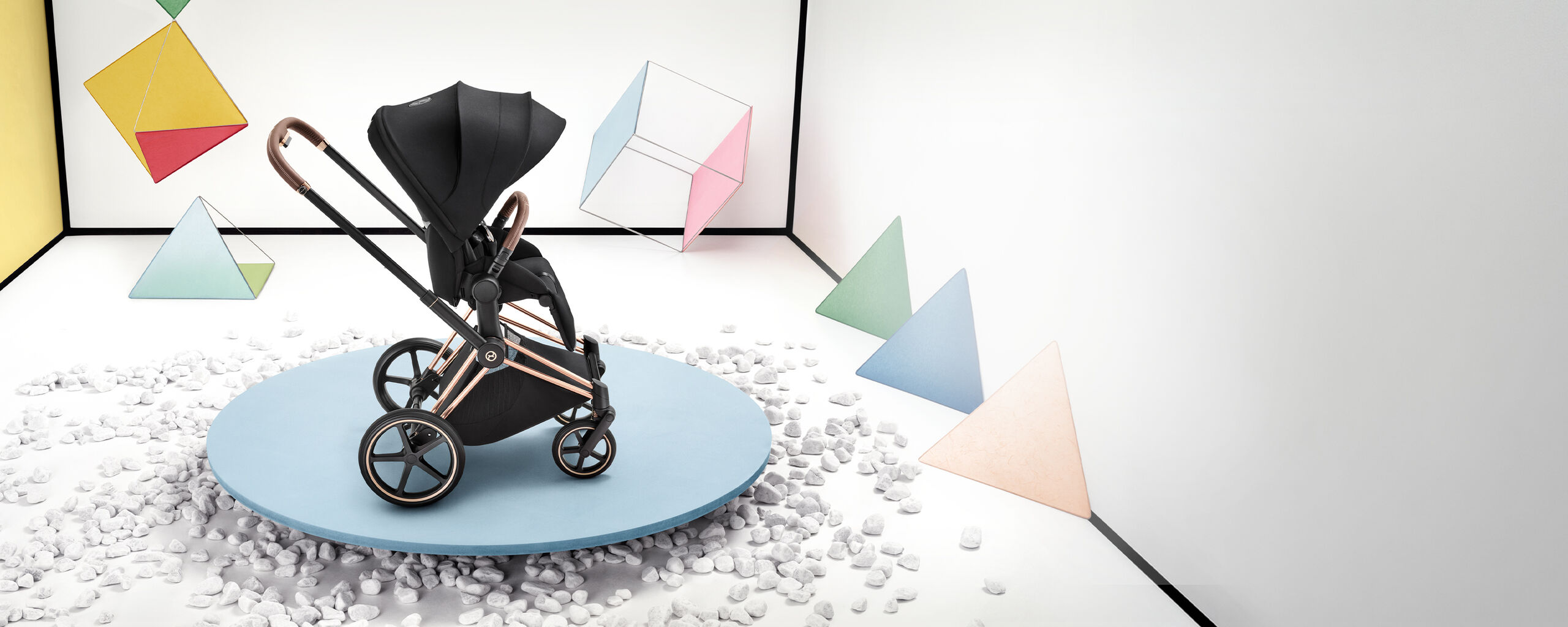 A Priam stroller on a pink thin platform. Various shapes and forms scattered behind and next to it.