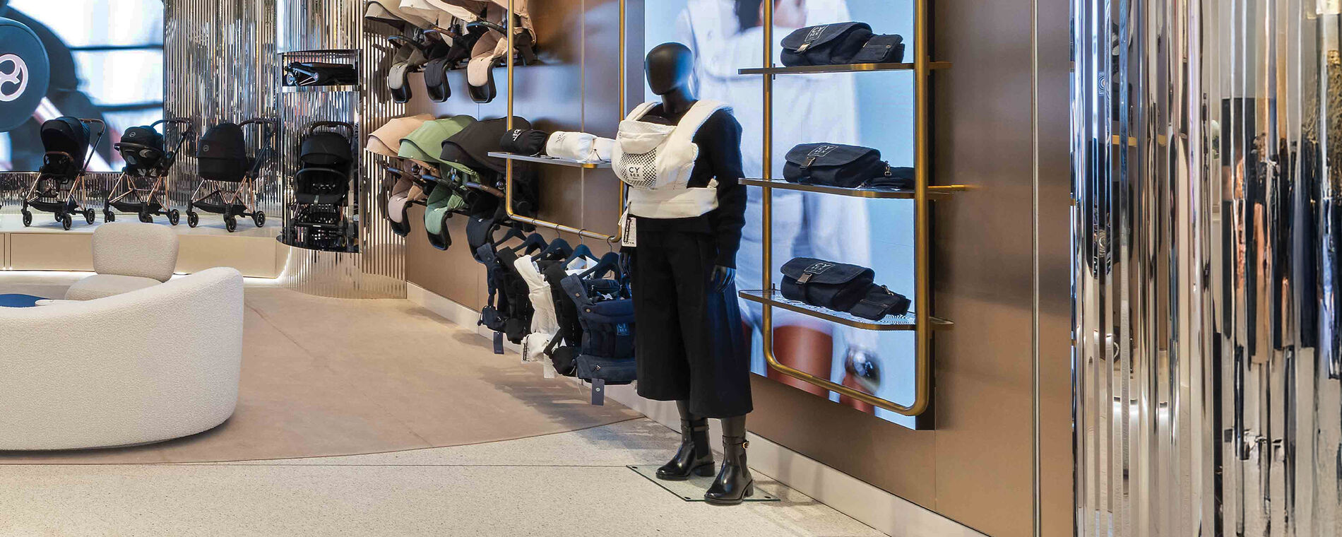 A mannequin holding a CYBEX Urban Mobility carrier. Several carriers, seat packs and strollers on display behind it.