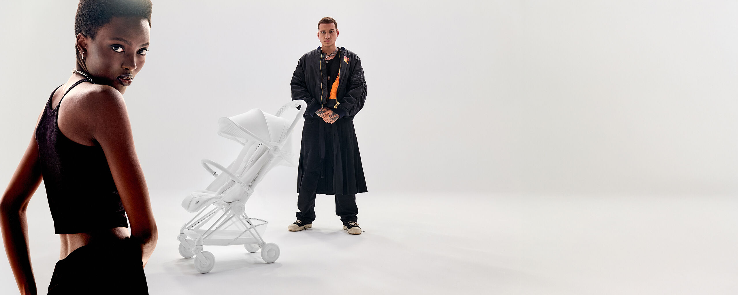 A woman in the front, a CYBEX Urban Mobility Coya in white behind her and a man behind the lightweight stroller.