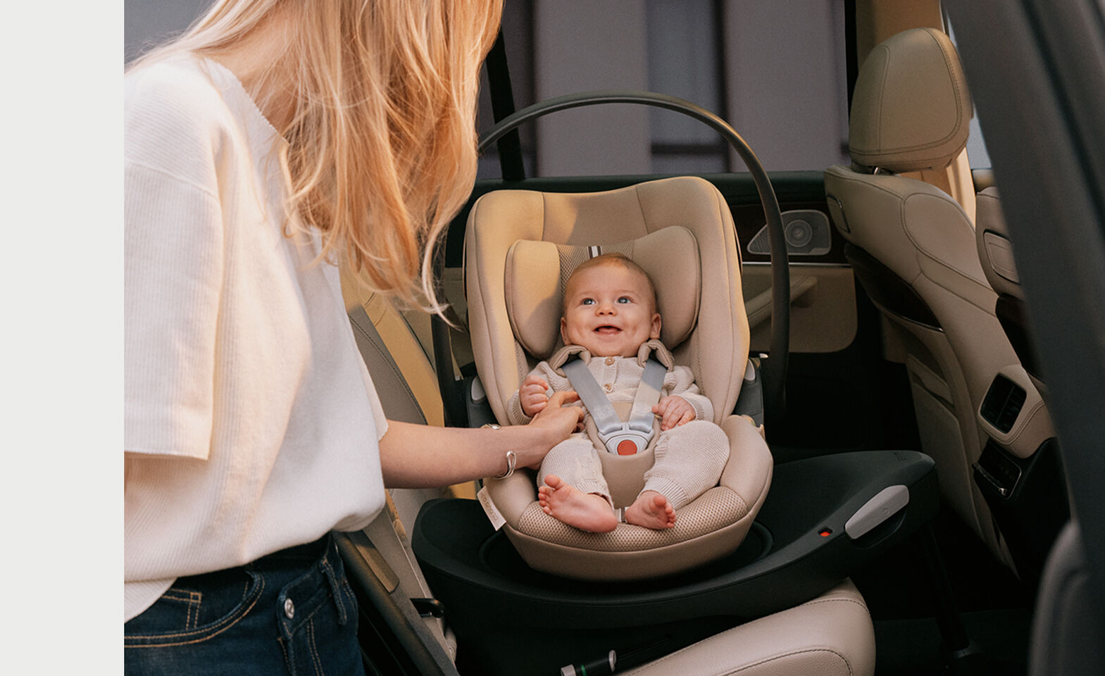 A mother tickles her infant sitting in the Cloud G3 in Almond Beige while smiling. The car seat is rotated towards the door. 