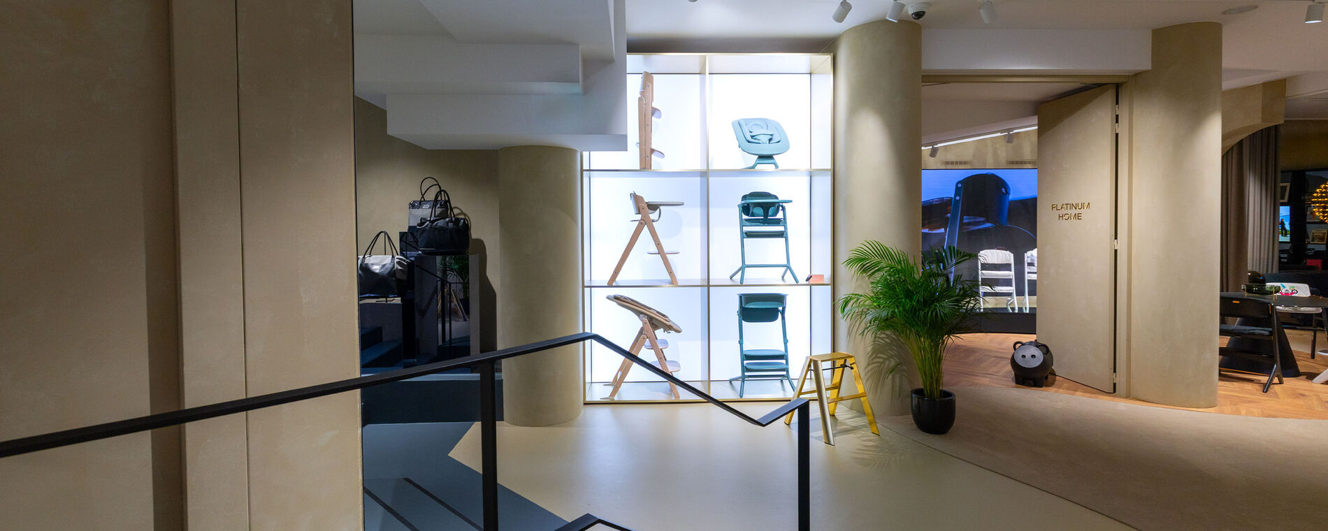 CYBEX store interior: display of various high chairs and bouncers on the wall, highlighted with backlighting.