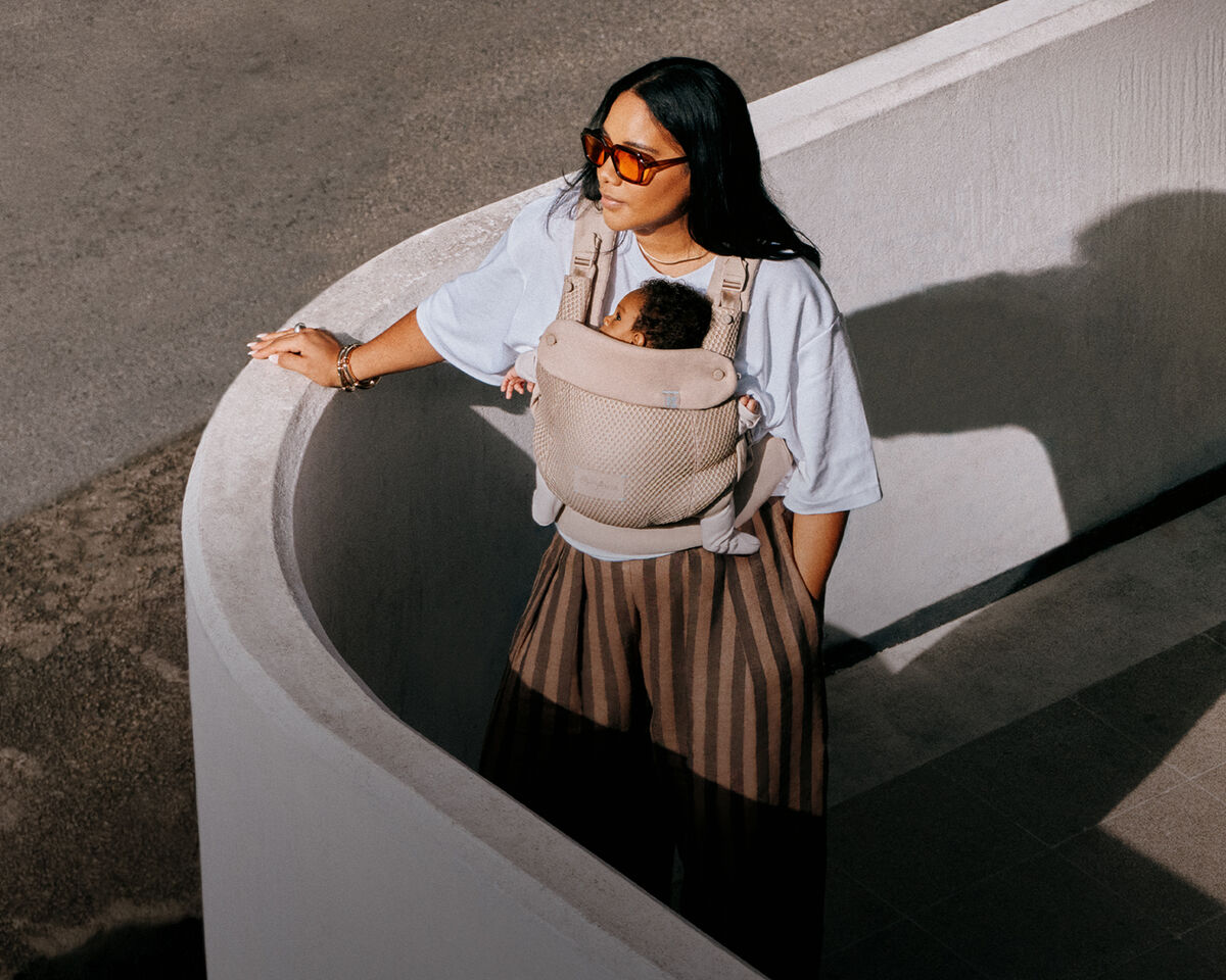 A woman standing with her arm leaning against the handlebar of her Balios S Lux stroller. With her other hand, she's holding her baby.
