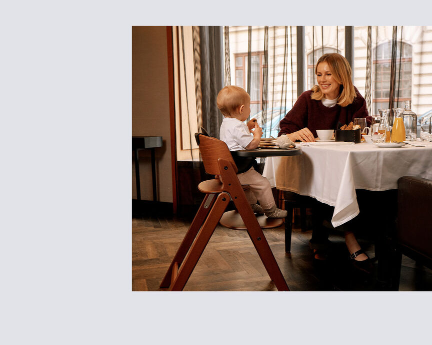 Woman smiling at a child seated in a CYBEX high chair at a restaurant table.