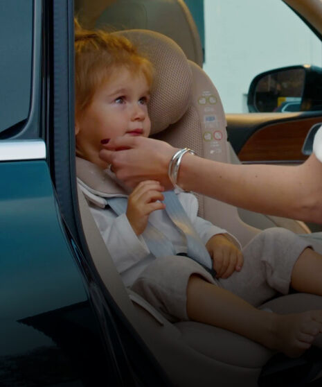 Ein Kind sitzt im Kindersitz zur Autotür hin, die Hand der Mutter stützt das Kinn.