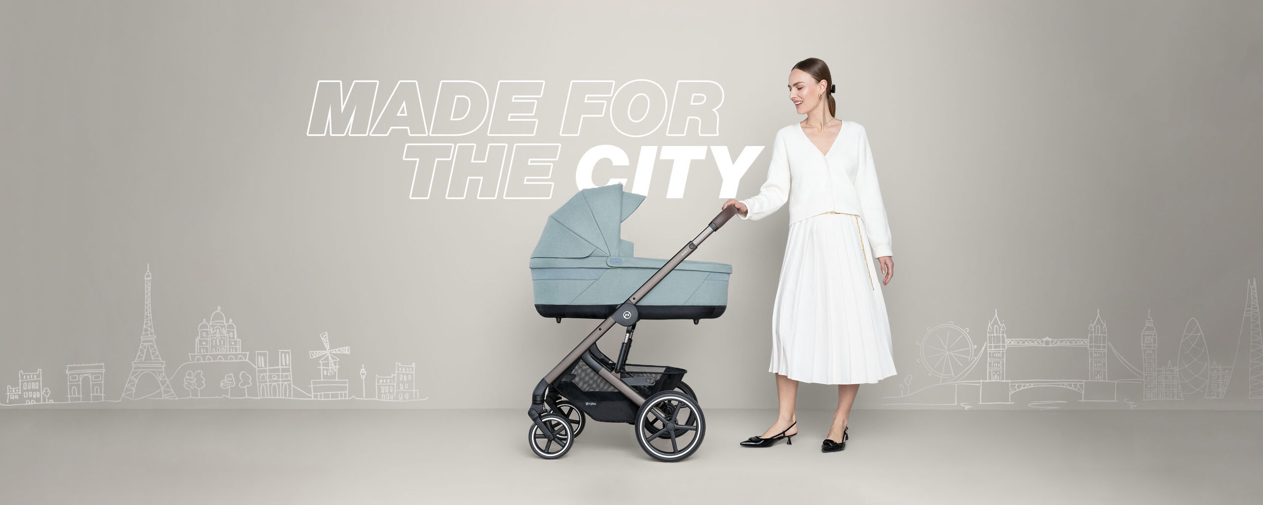 A woman in a white dress pushes a Balios S Lux city stroller against a beige background with the text "MADE FOR THE CITY".