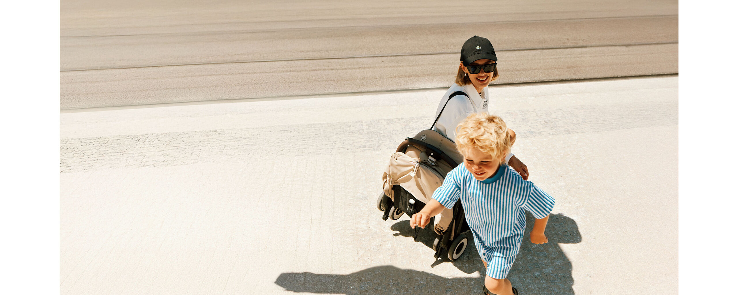 Aus der Vogelperspektive: Eine Mutter mit CYBEX Kinderwagen &uuml;ber der Schulter und ihr lachendes Kind &ndash; Mobilit&auml;t und Freude im Familienalltag.