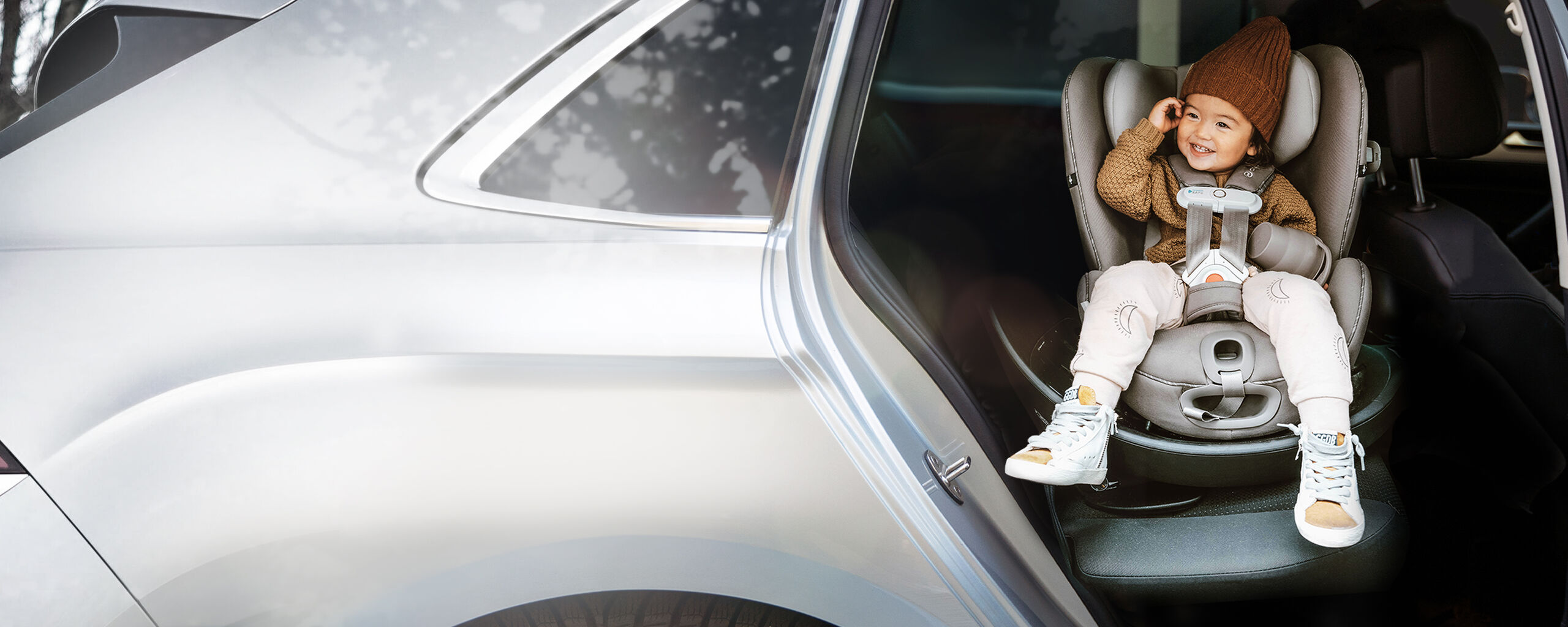 A smiling child sits in a car seat inside a parked car.