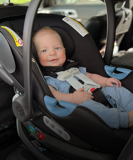 A baby sitting inside an infant car seat, smiling into the camera.