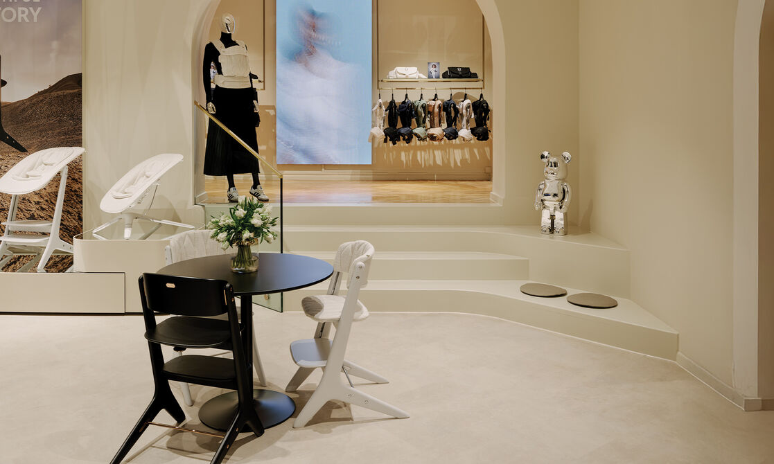 Three CYBEX chairs pushed against a round table. Behind is a set of stairs leading to the baby carrier section.