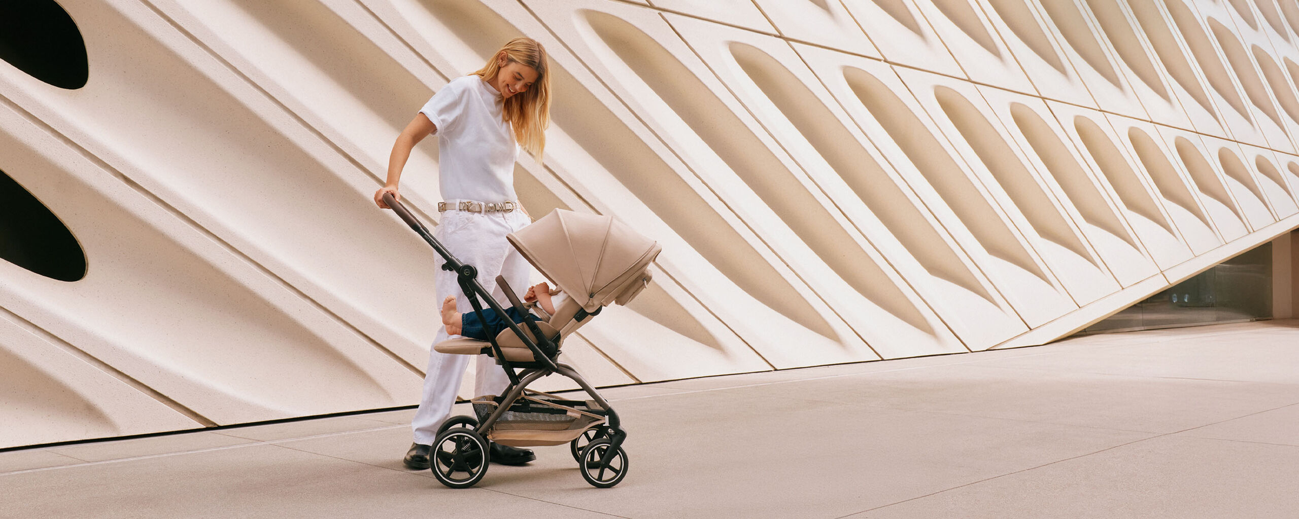 A man stands at a street corner pushing the Eezy S Twist +2 360 stroller, designed for both forward and rear-facing use.