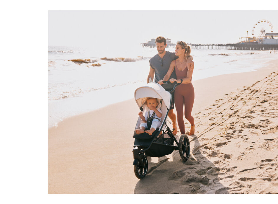 Parents pushing their child in an Avi Spin pushchair through the sand at the beach.