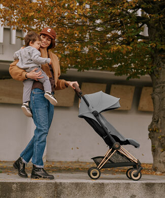 Matka drží syna a směje se na něj, zatímco jednou rukou tlačí golfový kočárek CYBEX.