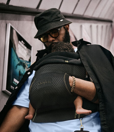 A man looking down at his baby in the Laya baby carrier, a jacket draped over his shoulders.