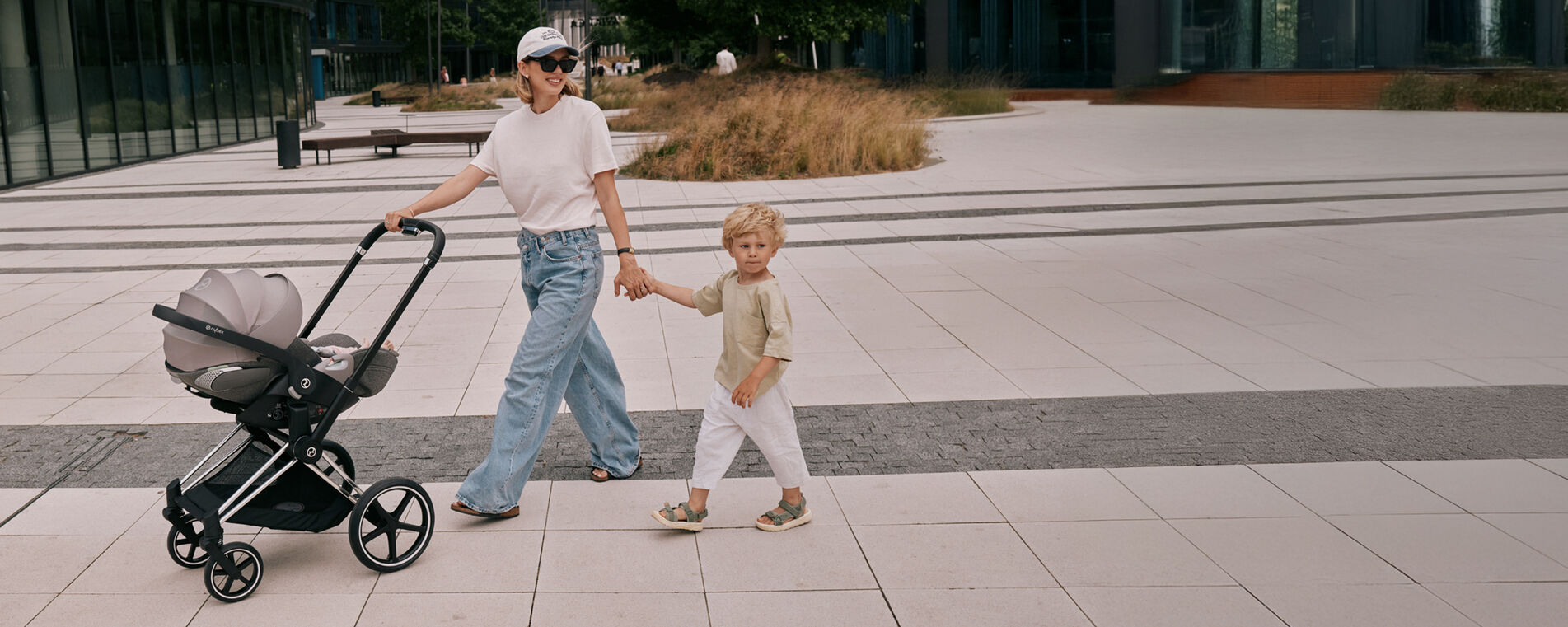 A mother pushing her CYBEX stroller with an attached Cloud T. She's holding the hand of her son with her free hand.