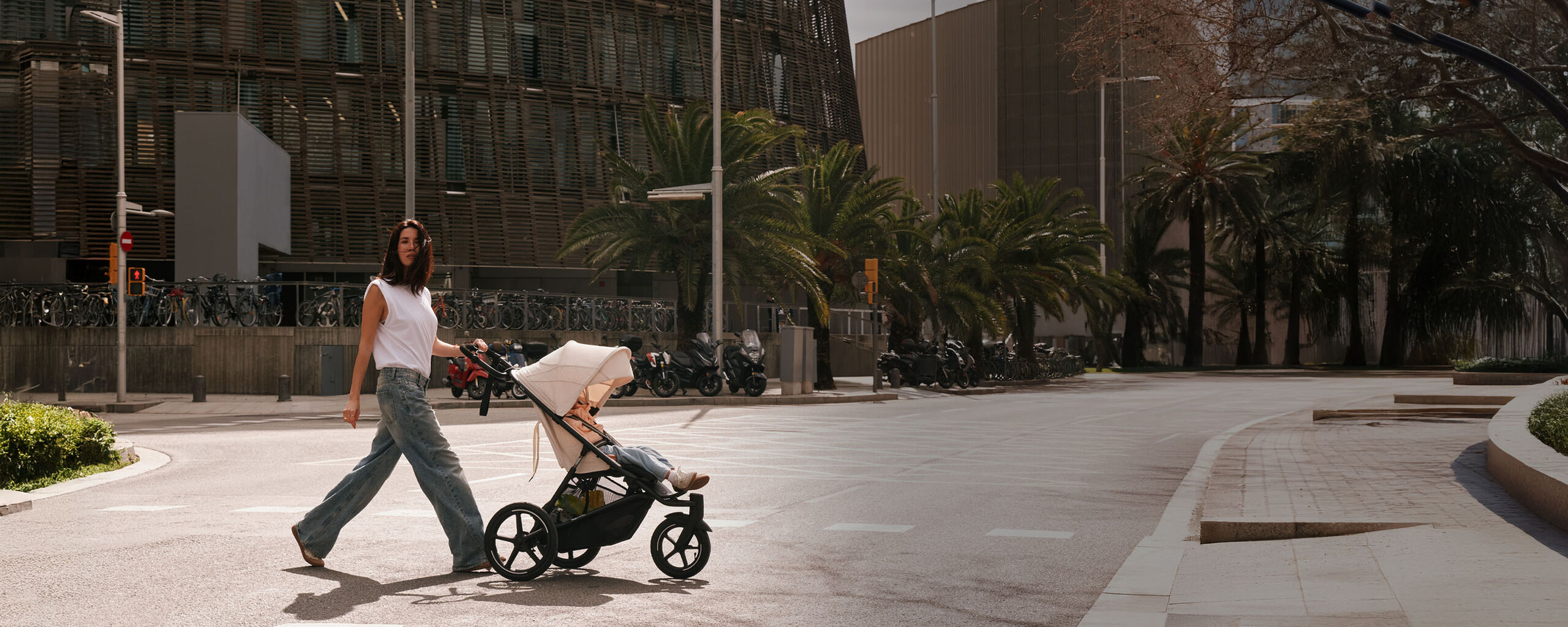 Uma mulher empurra um carrinho Avi Spin com um assento acoplado pela rua abaixo.