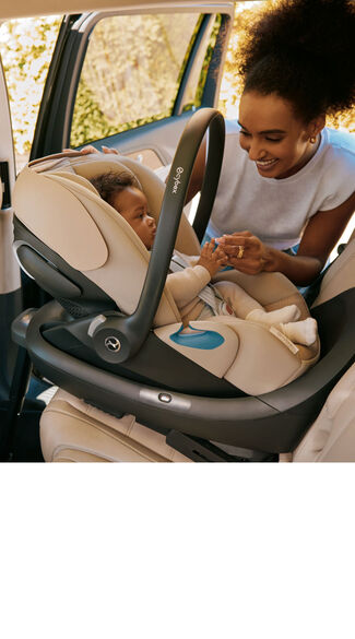 A woman smiling and holding their baby&rsquo;s hands while the baby sits secured in a CYBEX infant car seat inside a vehicle.