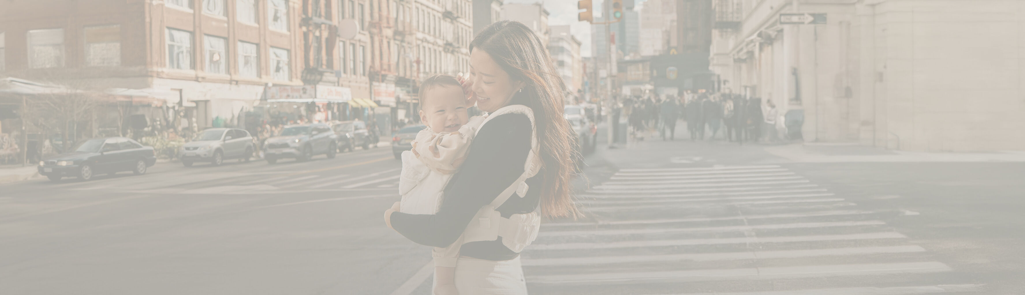 Žena stoj&iacute; na ulici v New Yorku a usm&iacute;v&aacute; se na sv&eacute; miminko v dětsk&eacute;m nos&iacute;tku.