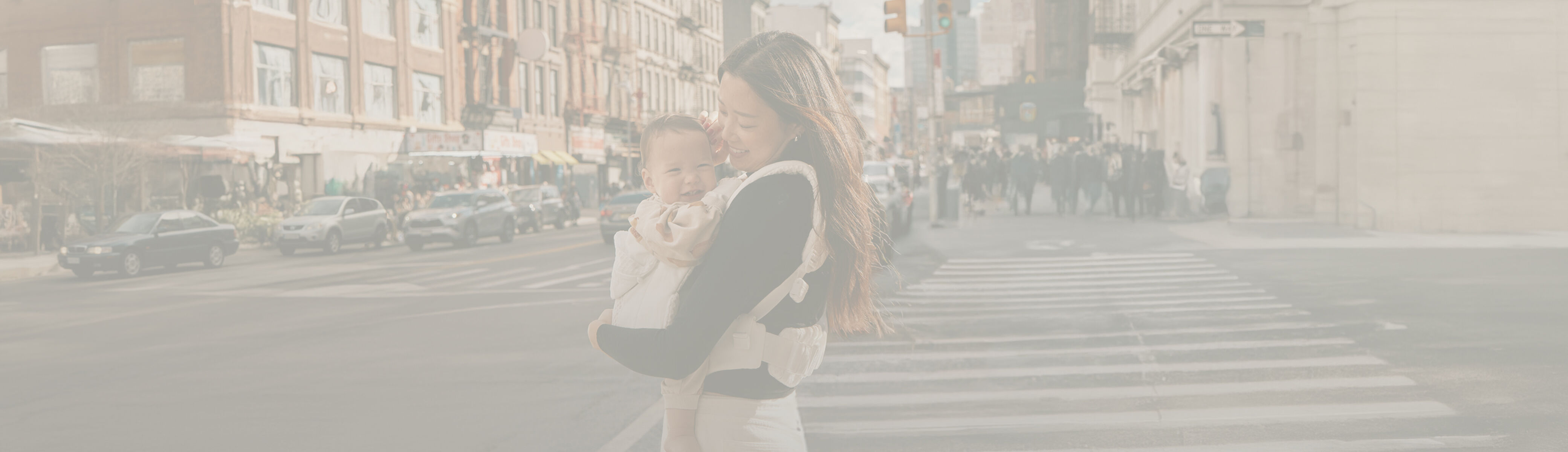 A woman standing on the streets of New York, smiling down at her baby in a baby carrier.