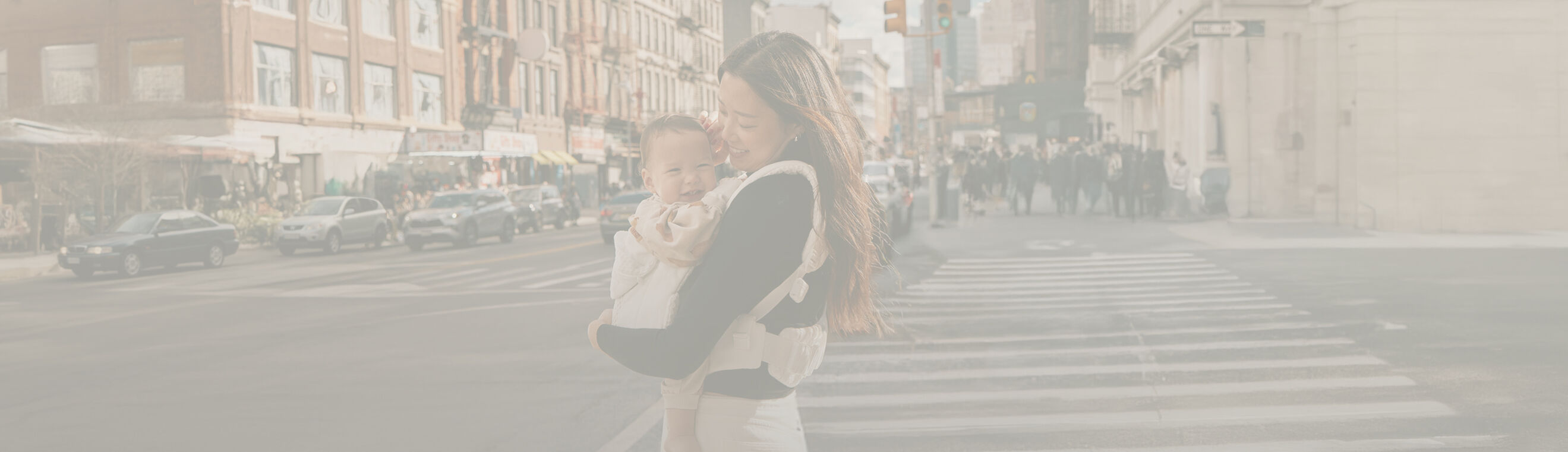 A woman standing on the streets of New York, smiling down at her baby in a baby carrier.