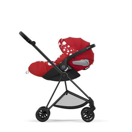 Red pram with white polka dots and black frame, side view.
