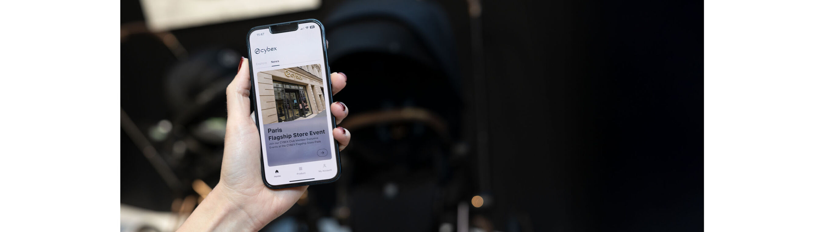 Detail shot: hand holding a smartphone displaying an image of the CYBEX Paris store, set against a blurred black background.