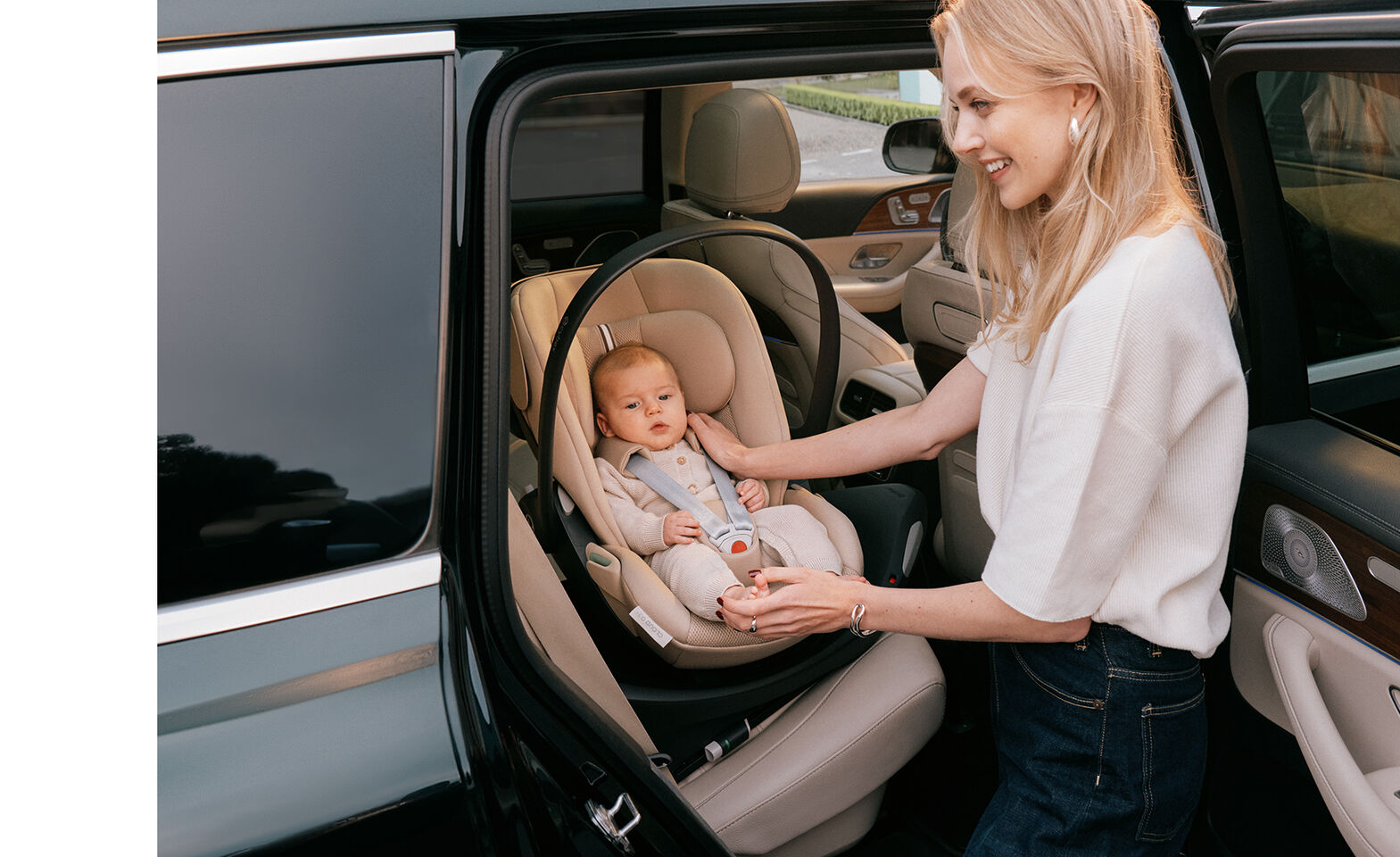 A mother is standing outside her car, one hand on the shoulder of her baby, the other holding their foot while the baby is lying in a rotated Cloud G3 infant car seat. 