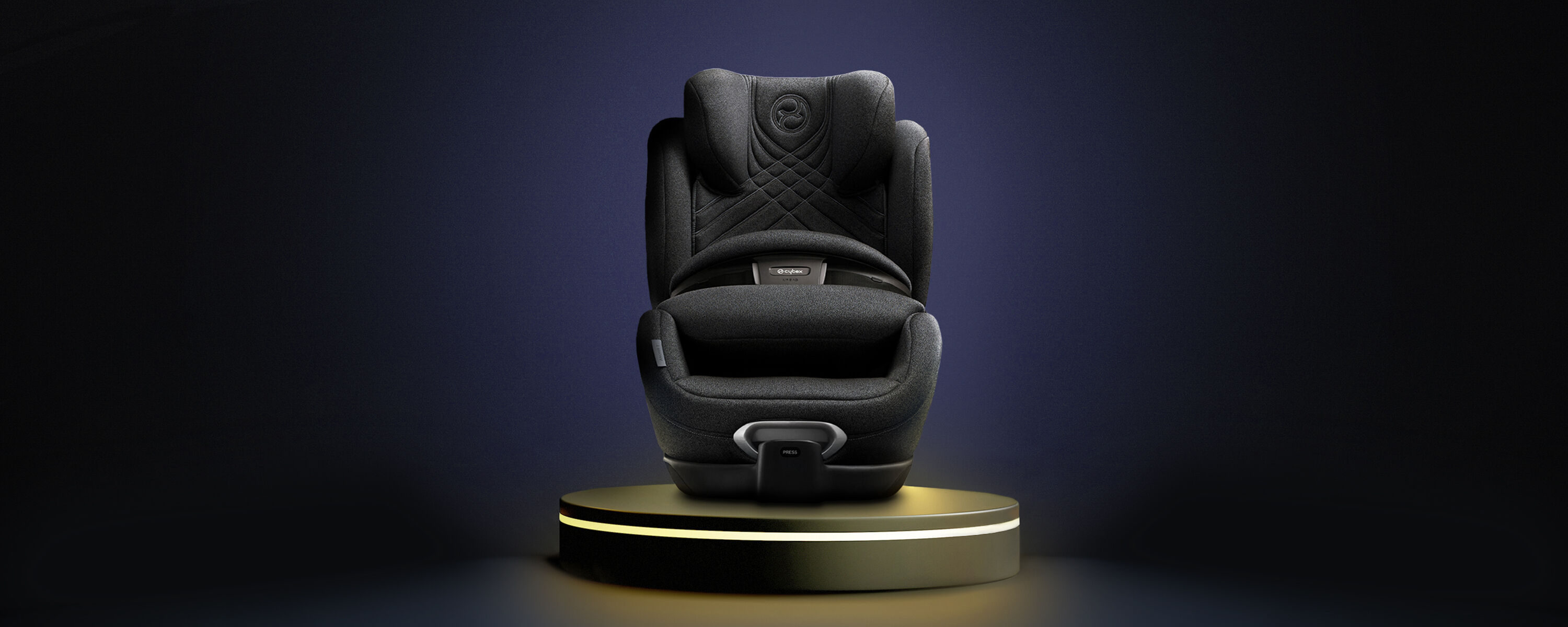Een moderne zwarte kinderautostoel op een verlicht voetstuk tegen een donkere achtergrond.