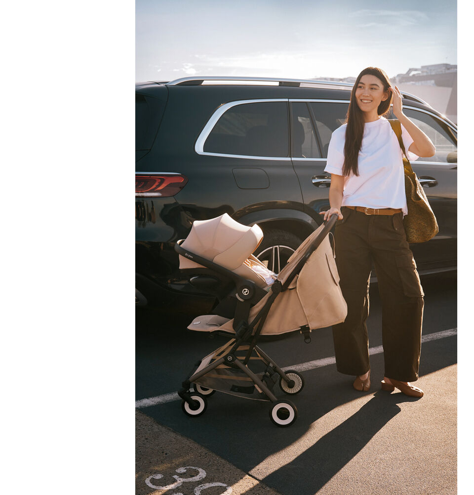 Frau steht neben einem Auto mit Orfeo Buggy und befestigter Babyschale