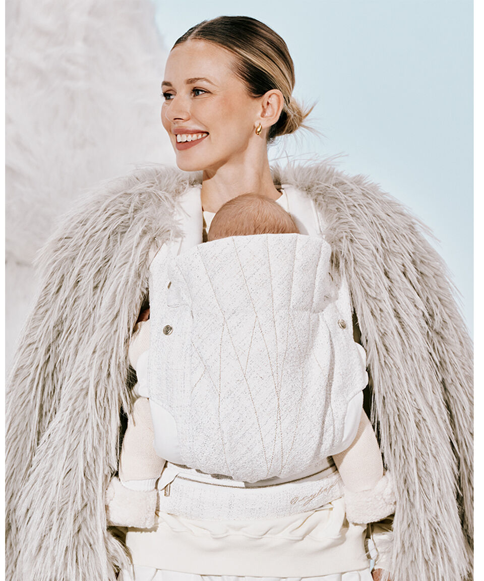 A woman grinning, looking to the left as she holds her baby in a CYBEX carrier.