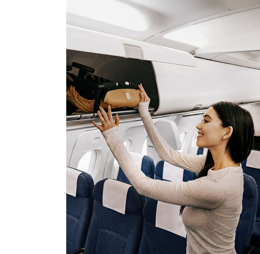 Een vrouw die een opgevouwen Libelle in het bagagevak boven haar hoofd in het vliegtuig opbergt.