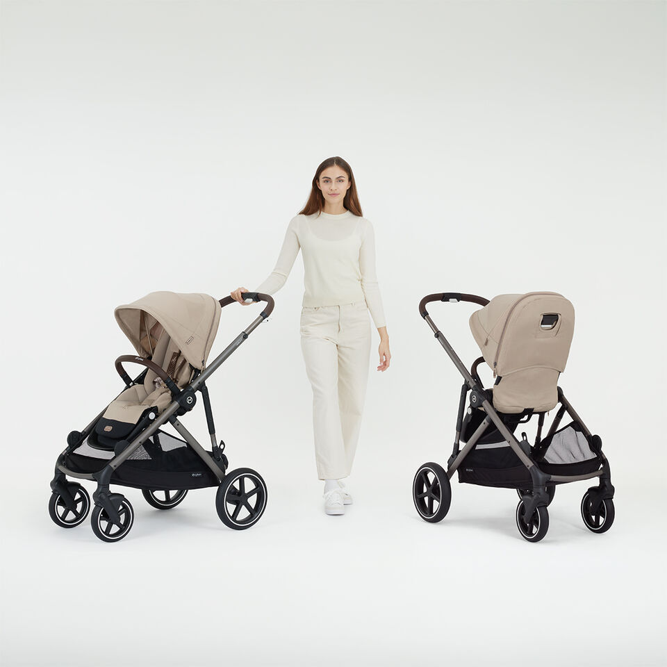 A woman standing next to two Gazelle S strollers, one with a forward facing seat unit, one with a rear facing one.