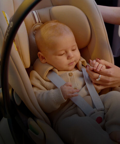 Ein Baby sitzt in einer Babyschale und hält die Hand seiner Mutter.