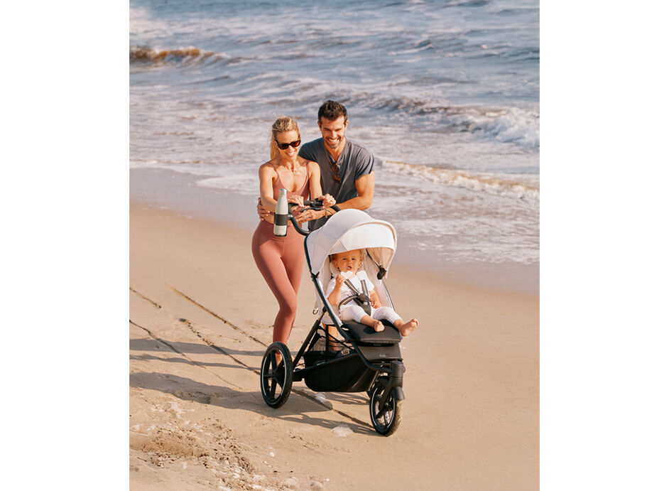 Parents laughing as they are pushing their Avi Spin stroller through the sand at the beach.