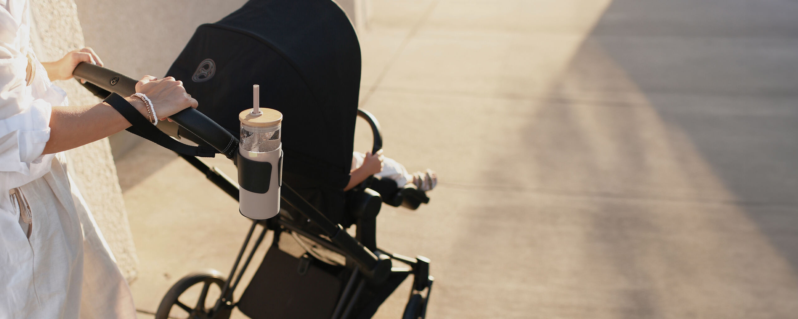 Une personne poussant une poussette avec un porte-gobelet sur le c&ocirc;t&eacute;.