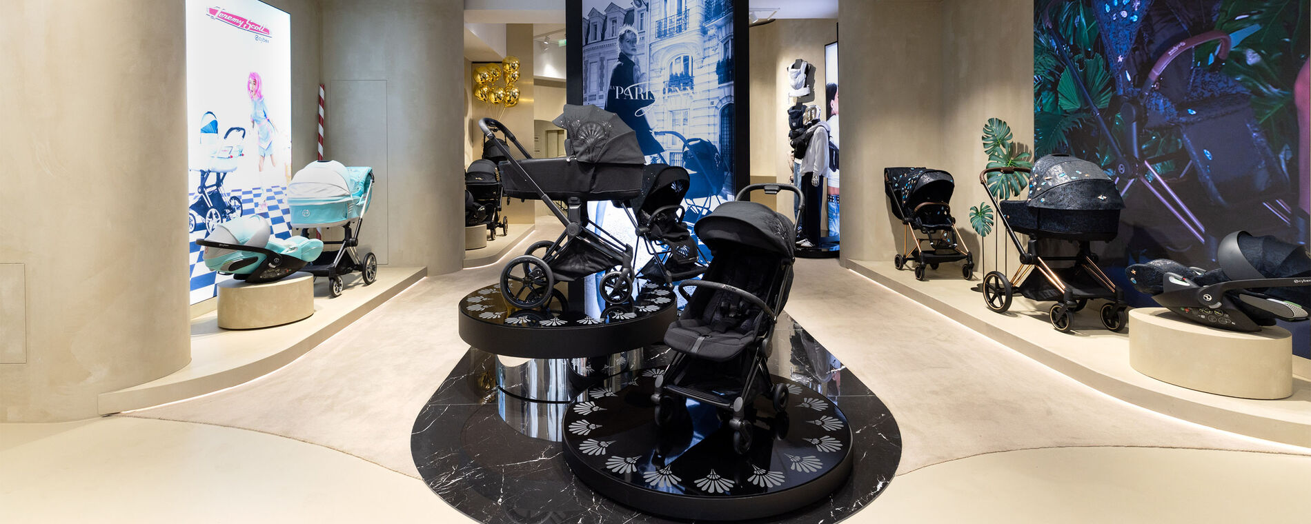 CYBEX store interior featuring the La Parisienne collection displayed on black marble in the centre. On the left and right, additional exclusive pushchair designs are showcased: the Jeremy Scott Car collection and the Jewels of Nature collection.